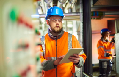 Technicien avec un casque et gilet orange en intervention avec tablette